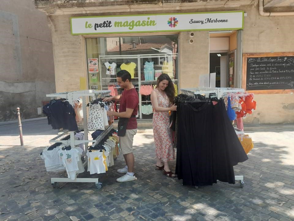 un homme et une femme regardent des vêtements présentés devant le petit magasin